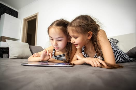 Closeup portrait of two sisters lying on bed with tablet