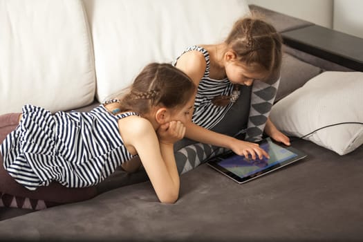 Two sisters with tablet on couch at home