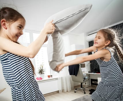 Closeup portrait of two little sisters fighting with pillows