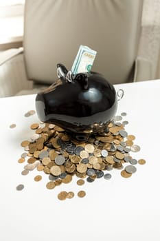 Closeup photo of black piggy bank standing on pile of coins on white table