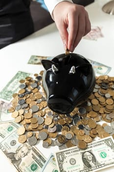 Closeup photo of hand putting coin in black piggy bank