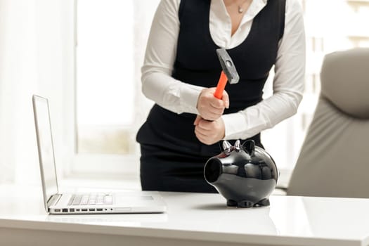 Closeup photo of woman breaking piggy bank at office with hammer