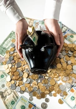 Closeup photo of woman holding black pig moneybox on pile of coins