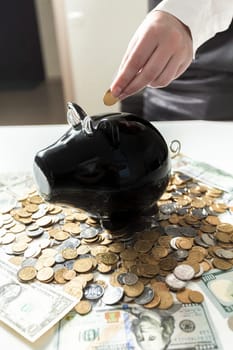 Young businesswoman putting coin in black piggy bank