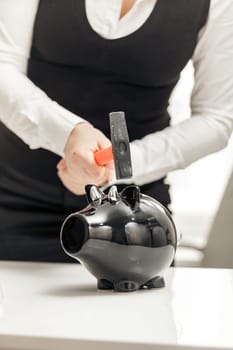 Young businesswoman hitting piggy bank with hammer