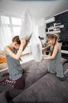 Two young sisters pillow fighting on couch