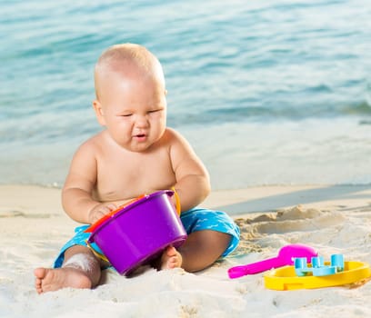 Cute baby on the tropical beach playing toys