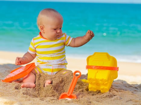 Cute baby on the tropical beach playing toys