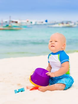Cute baby on the tropical beach playing toys