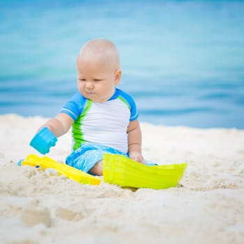 Cute baby on the tropical beach playing toys