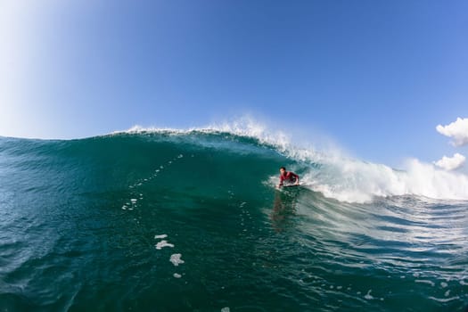 Surfing bodyboarder rides ocean blue wave crashing breaking onto reef beach shallows, a water photo perspective.