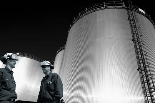 two oil and gas workers with large industrial fuel storage tanks