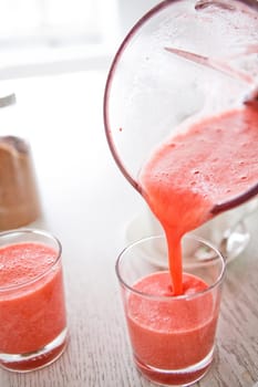 Closeup of delicious strawberry smoothie being poured into a glass from a large jug