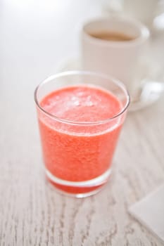 Closeup of strawberry smoothie in glass with cup of coffee in background