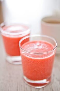 Closeup of two glasses of strawberry smoothies with cup of coffee in background