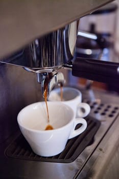 Closeup of professional standard espresso machine in cafe with coffee filtering into two cups from brewing group