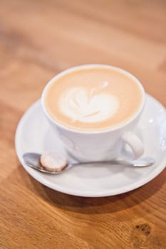 Closeup of espresso and milk based latte in cup with apple shape coffee art design on wooden table