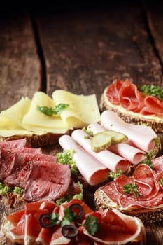 Assorted meat and cheese sandwiches with rare roast beef, mortadella, ham, gouda, salami, on rye and wholewheat bread on a rustic wooden table with copyspace