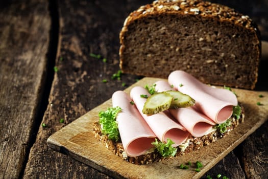 Mortadella sandwich on wholewheat bread with slices of traditional German ground pork and beef sausage topped with gherkin and fresh parsley