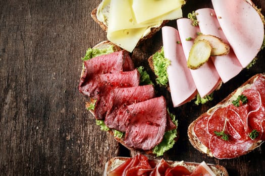 Buffet with assorted open sandwiches displayed at a restaurant with gouda cheese, rare roast beef, ham, mortadella and salami on a rustic wooden table with copyspace