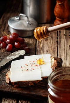 Drizzling golden honey onto a goats milk cheese sandwich while preparing a healthy breakfast in a country kitchen