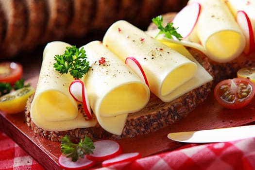 Tasty gouda cheese sandwich on wholegrain bread topped with slice radish and parsely for a healthy country lunch, close up view
