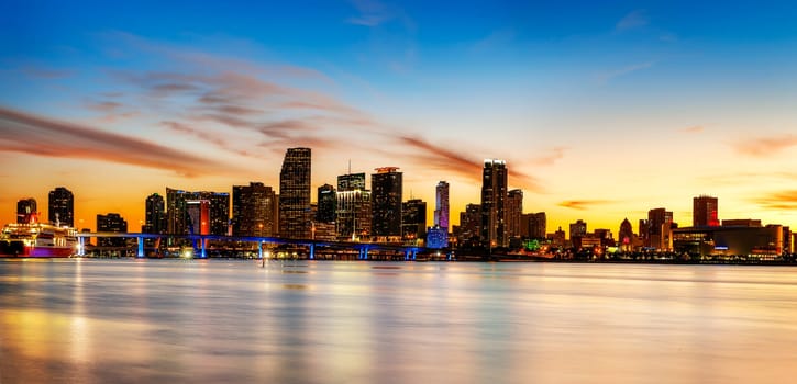 Miami city skyline panorama at dusk with urban skyscrapers over sea with reflection