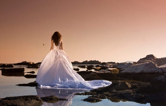 Vintage photo of beautiful bride standing on a cliff on the sea