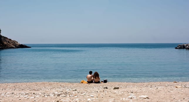 Vintage photo of a young couple sitting on the beach and looking at sea