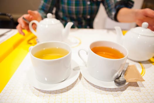 Closeup of two cups of herbal tea with tea pots and woman sitting in background