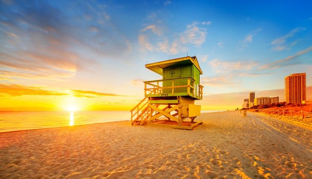 Miami South Beach sunrise with lifeguard tower and coastline with colorful cloud and blue sky.