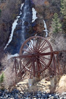 The Charlie Tayler Waterwheel with Bridal Veil waterfall in the background cascading down the mountainside into Clear Creek River on a spring day.