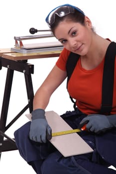 A woman measuring  a tile before cutting it.
