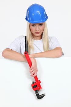 Woman stood by blank poster holding wrench