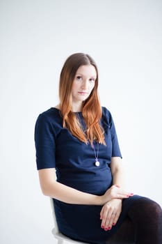 Studio portrait of thoughtful looking attractive woman wearing blue blouse and sitting in chair with hands resting on lap