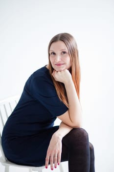 Studio portrait of happy smiling attractive woman wearing blue blouse and sitting in chair and resting chin on hand