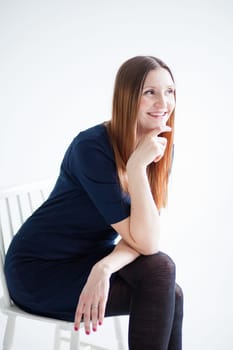 Studio portrait of happy smiling attractive woman wearing blue blouse and sitting in chair and holding hand to chin