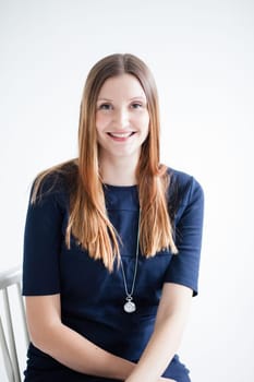 Studio portrait of happy smiling attractive woman wearing blue blouse and sitting in chair with arms crossed