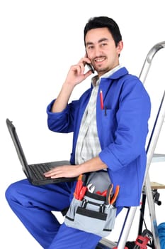 Plumber sat on step ladder holding mobile telephone