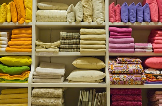 Bright pillows, towels, plaids, blankets and other home wear on shelves