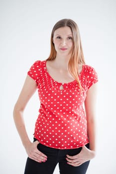 Studio portrait of attractive woman with happy smirk and wearing red blouse and standing with hands on hips