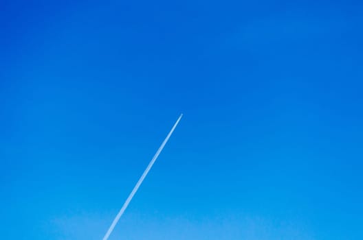 Plane leaves condensate strips in a cloudless sky.