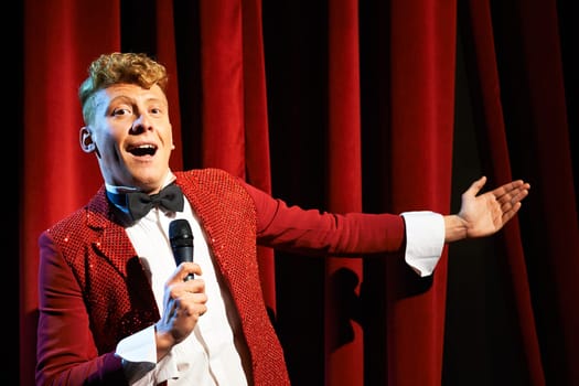 Arts and entertainment in theatre with funny man working as anchorman, standing against red curtains with microphone
