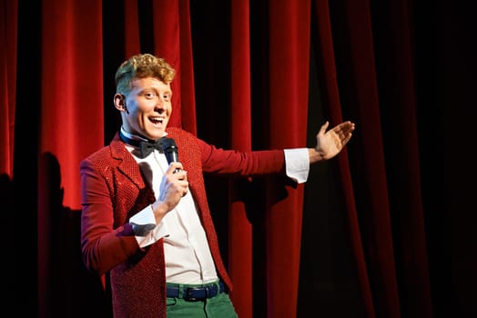 Arts and entertainment in theatre with funny man working as anchorman, standing against red curtains with microphone