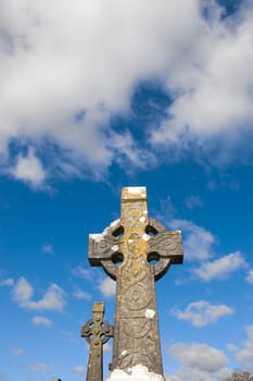 two old celtic crosses in an irish graveyard with blue cloudy sky
