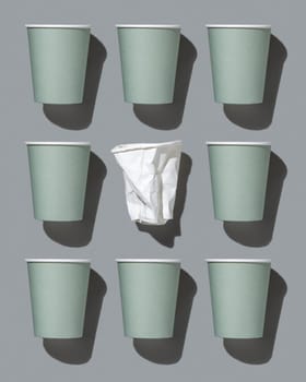 Disposable new light green paper cups and crumpled used white one on gray top view, pattern, hard shadow, mockup with copy space. Empty cardboard coffee cups flat lay. Consumerism concept