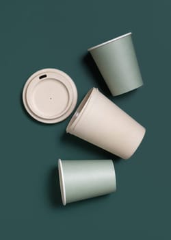Disposable new light green paper cups and reusable bamboo coffee cup in a line a dark green top view, mockup with copy space. Empty coffee cups flat lay. No plastic and sustainable lifestyle concept