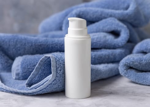 White blank one pump bottle near blue towel in bathroom closeup, brand packaging mockup. Natural handmade cosmetic product - cream, lotion or soap for daily face or handcare, copy space
