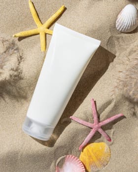 White blank cream tube, starfishes and seashells on a sandy beach top view, hard shadow. Sunscreen cosmetics mockup. Summer vacation with spf uv-protected sunbathing