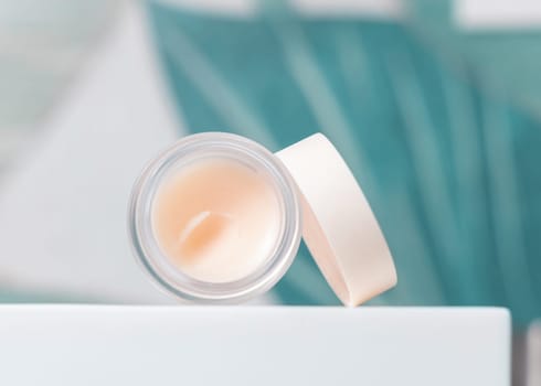 Opened white blank lip balm jar with a lid on washbasin with faucet in green tropical bathroom close up, packaging mockup. Lifestile scene with ubranded natural lipcare product